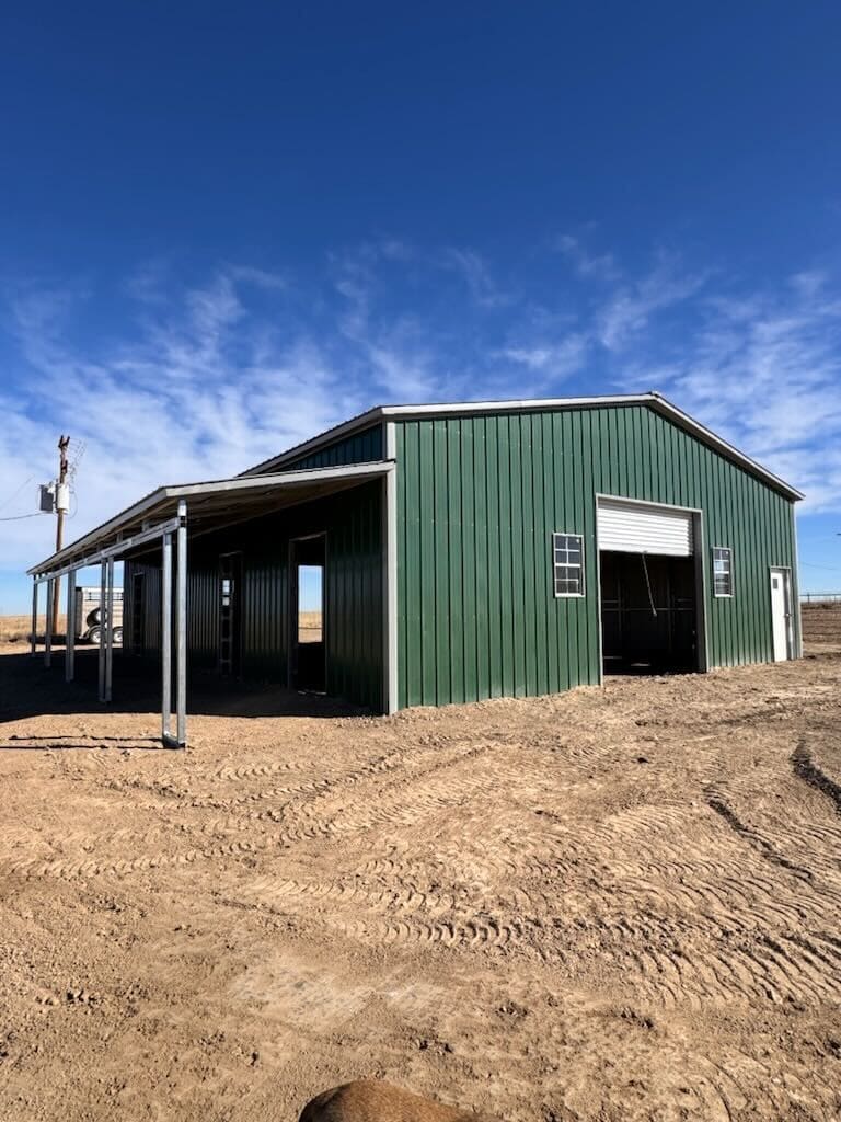 Green metal barn under clear blue sky.